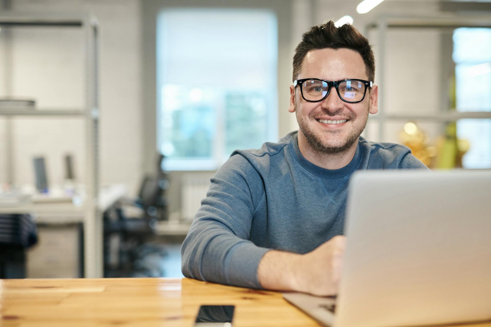 Henkilö Happy man wearing glasses working remotely on laptop in modern office environment.